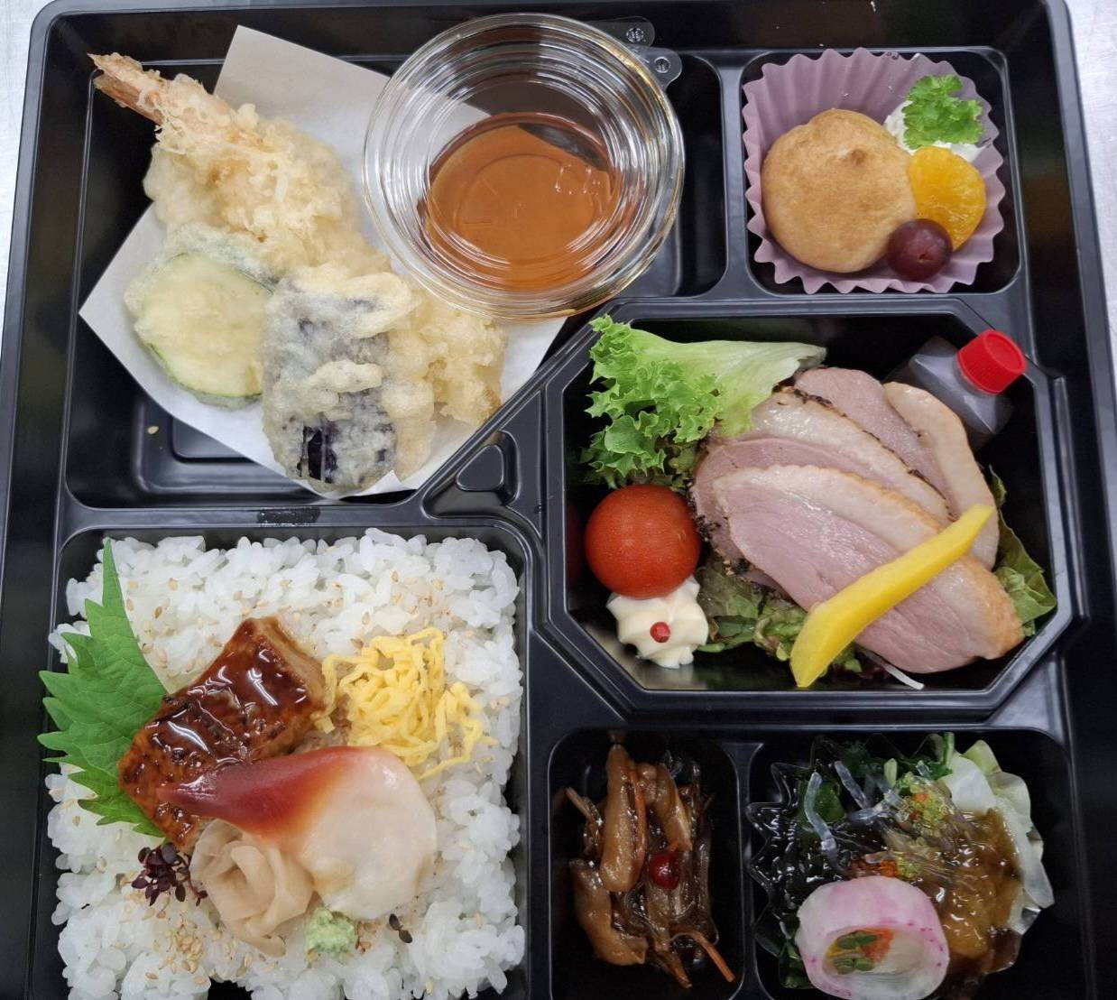 黒い折に詰めたお料理。天ぷら、鴨のロースト、鰻と酢飯、季節の小鉢、シュークリーム